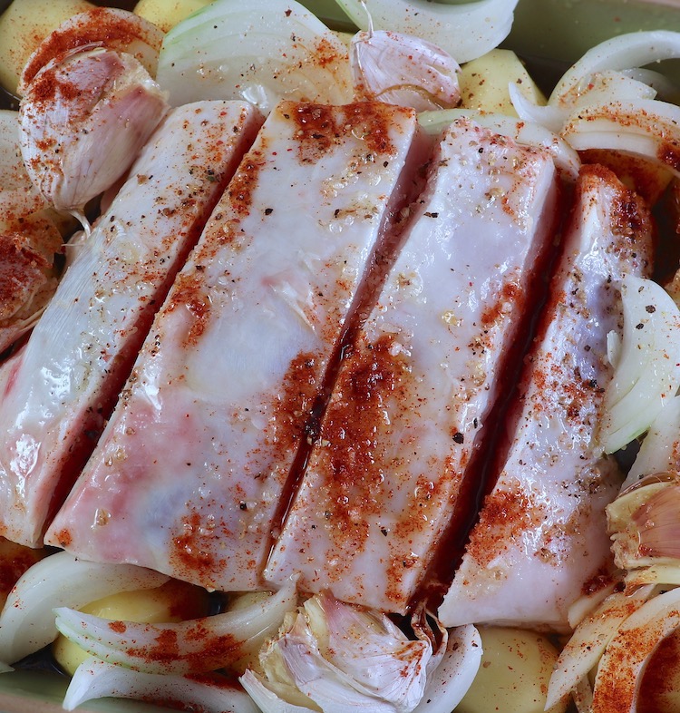 Pork loin on a baking dish with potatoes, onion, garlic, olive oil, white wine, salt, pepper, and paprika