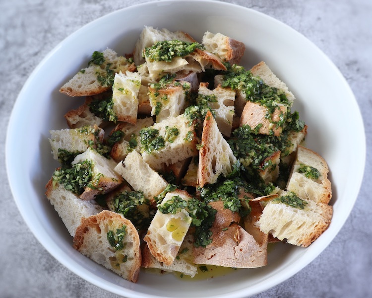 Bread cut into pieces drizzled with olive oil and coriander mixture on a large bowl