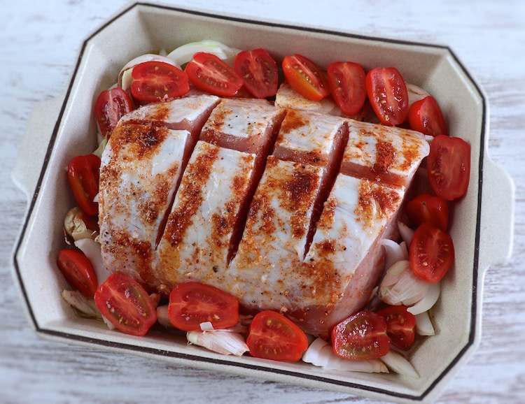 Pork loin on a baking dish seasoned with salt, pepper, paprika, onion, garlic, grape tomato and olive oil