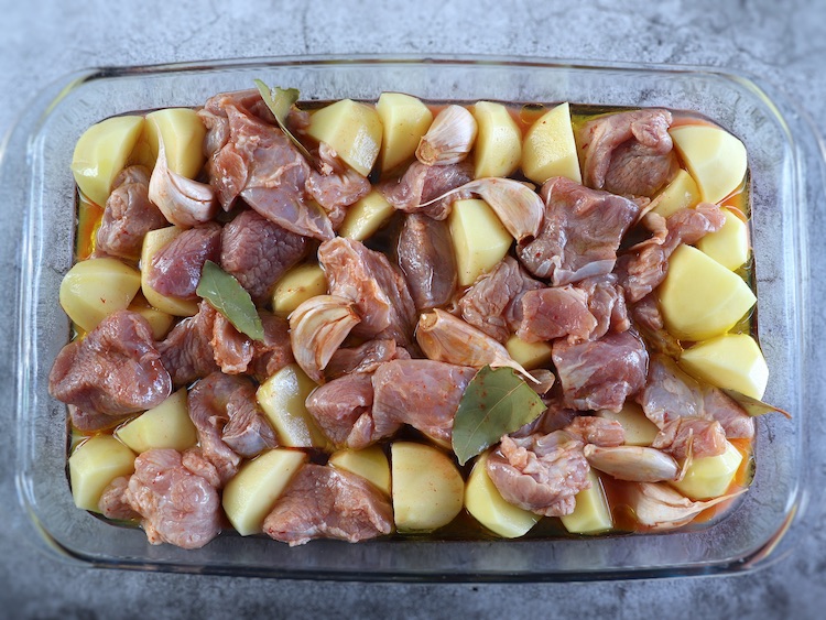 Pork and potatoes seasoned with salt, garlic, bay leaf, sweet red pepper paste, white wine and olive oil on a glass baking dish