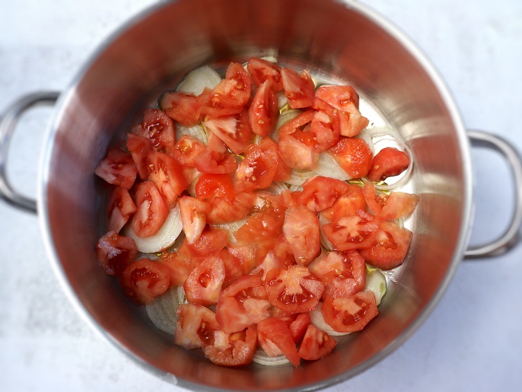 Azeite, cebola cortada às rodelas e tomate sem pele cortado em pequenos pedaços num tacho