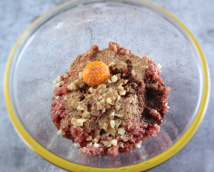 Ground meat seasoned with salt, nutmeg, pepper, chopped garlic, Worcestershire sauce, egg yolk and breadcrumbs on a large glass bowl