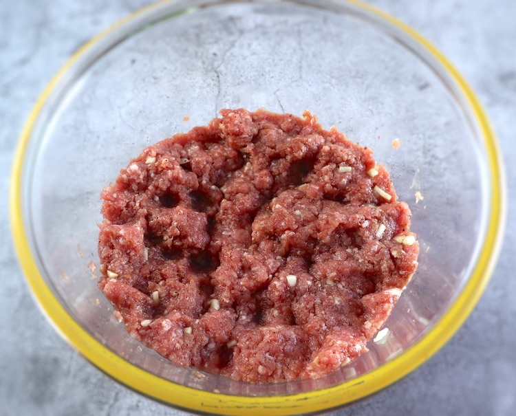 Ground meat mixed with salt, nutmeg, pepper, chopped garlic, Worcestershire sauce, egg yolk and breadcrumbs on a large glass bowl