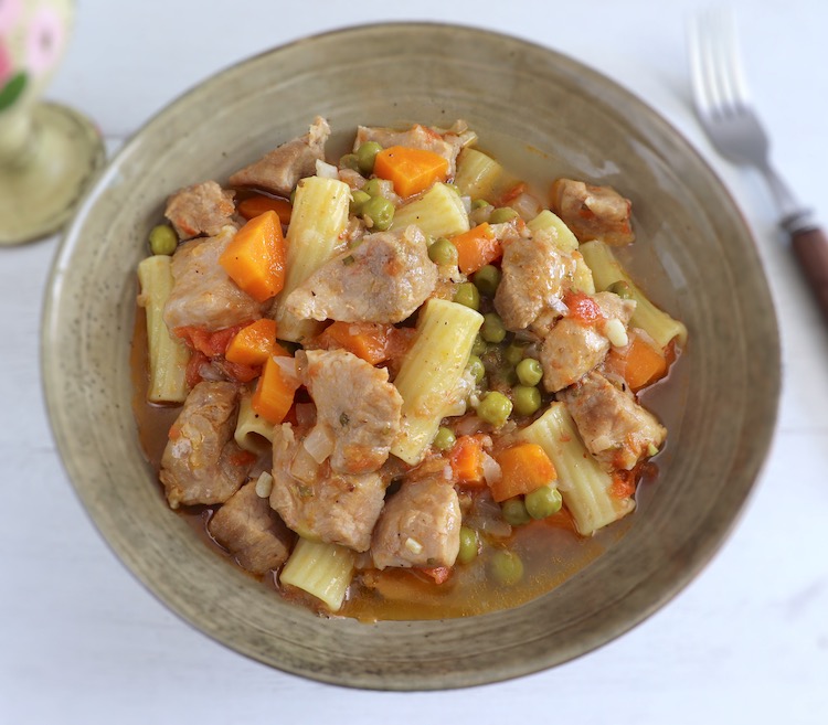 Carne de porco guisada com ervilhas, cenoura e massa num prato fundo