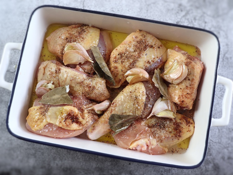 Chicken seasoned with white wine, salt, pepper, nutmeg, unpeeled crushed garlic, bay leaf and olive oil on a baking dish