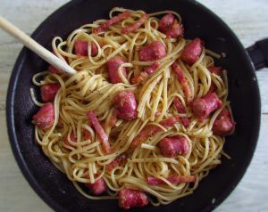 Spaghetti with fresh sausage and bacon on a frying pan