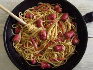 Spaghetti with fresh sausage and bacon on a frying pan