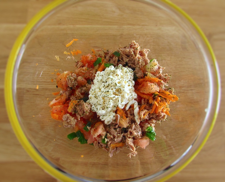 Shredded tuna, grated carrot, pepper cut into small pieces, tomato pieces and mayonnaise on a glass bowl seasoned with pepper and dried coriander leaves