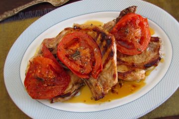 Costeletas de porco grelhadas com tomate numa travessa