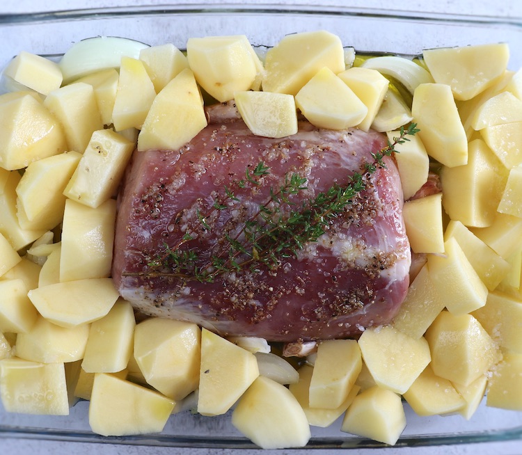 Pork loin and potatoes seasoned with white wine, salt, pepper, unpeeled crushed garlic, thyme, onion and olive oil on a glass baking dish