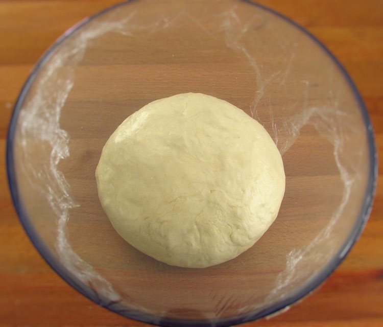 Garlic bread dough on a glass bowl covered with cling film