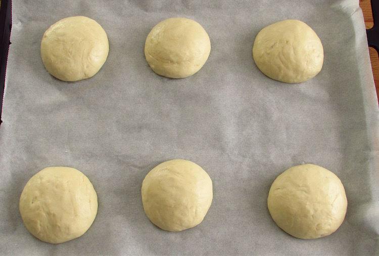 Garlic bread dough divided in six balls on a baking tray lined with tracing paper