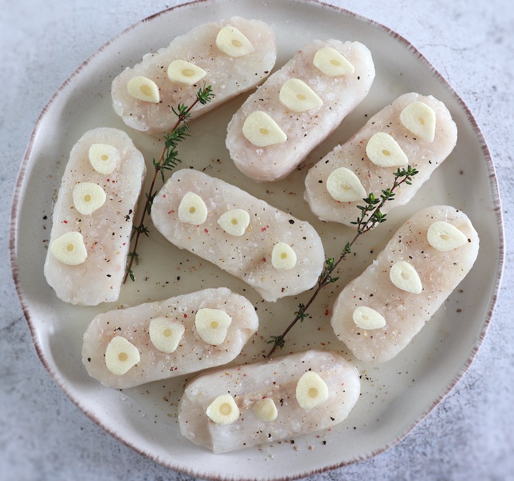 Lombos de pescada temperados com sumo de limão, sal, pimenta, alhos laminados e tomilho num prato