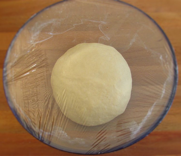 Milk bread dough sprinkled with flour on a glass bowl covered with cling film