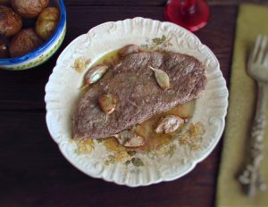 Steak in the oven on a plate with unpeeled potatoes