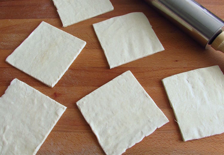 Puff pastry cut into squares on a wooden table