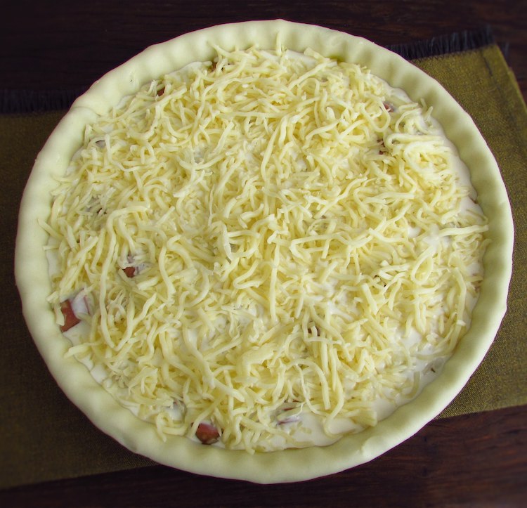 Pie filled with ham and sausage mixture, drizzled with béchamel and sprinkled with grated cheese