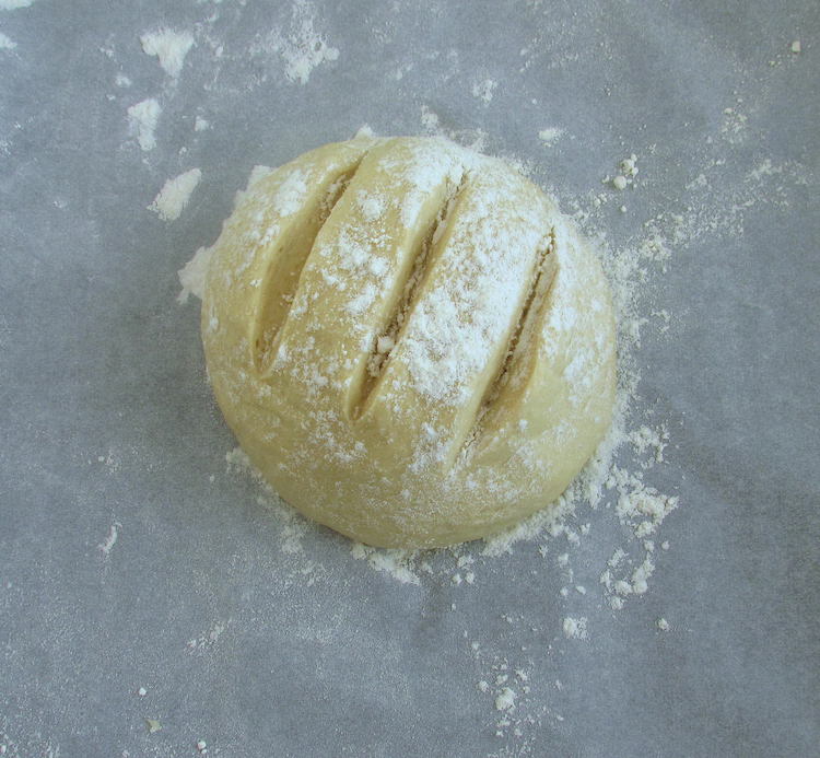 Massa de pão em forma de bola polvilhada com farinha num tabuleiro forrado com papel vegetal