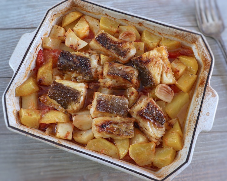 Baked cod with tomato and potatoes on a baking dish