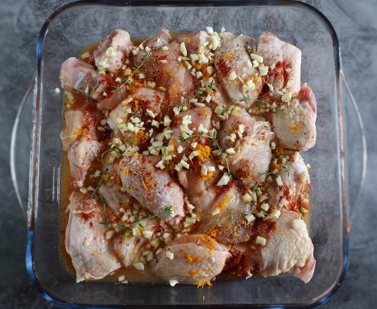 Chicken cut into pieces seasoned with orange and spices on a glass baking dish