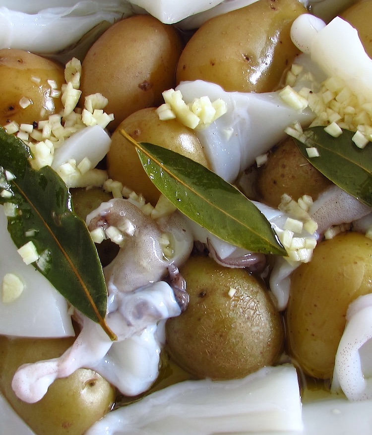 Cuttlefish and potatoes seasoned with salt, pepper, chopped garlic, bay leaf and olive oil on a baking dish