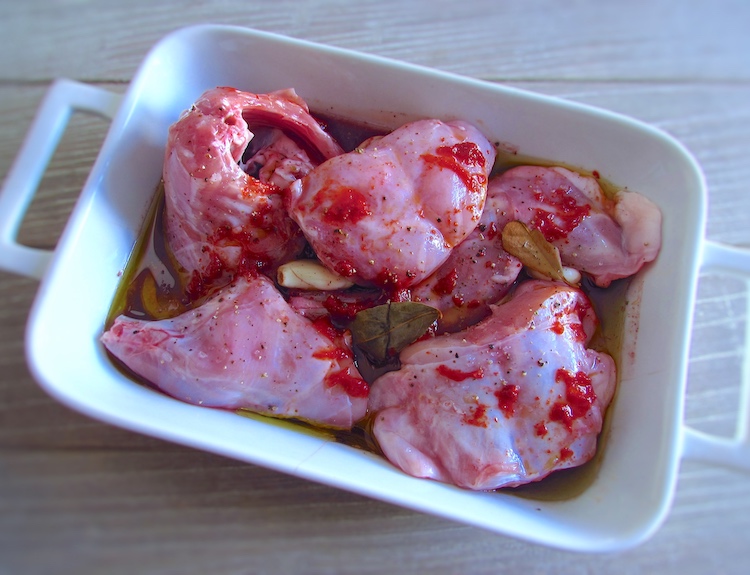 Rabbit seasoned with salt, peeled garlic, pepper, red pepper sauce, white wine, red wine, bay leaf and olive oil on a baking dish