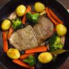 Steaks with potatoes and sautéed vegetables on a frying pan