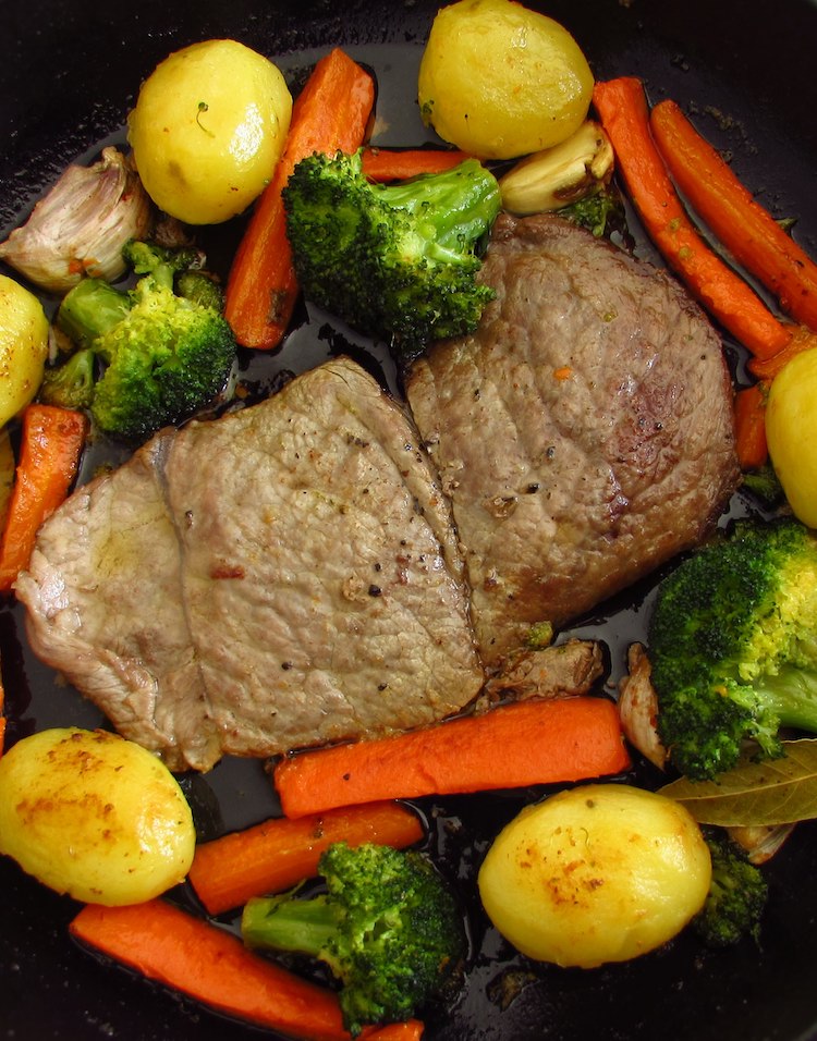 Steaks with potatoes and sautéed vegetables on a frying pan