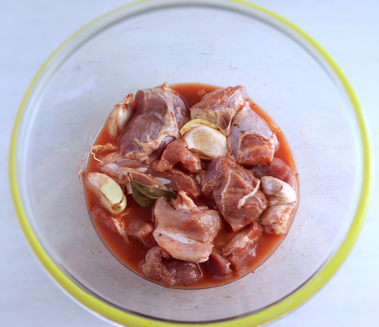 Pork cubes seasoned with salt, pepper, unpeeled crushed garlic, sweet red pepper paste, bay leaf and white wine on a glass bowl