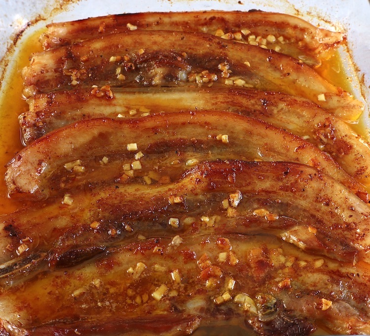 Roasted pork belly strips on a glass baking dish