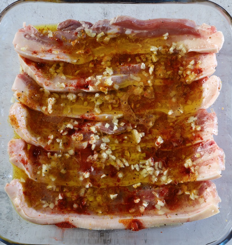 Pork belly strips seasoned with salt, curry, paprika, pepper, chopped garlic, lemon juice and honey on glass baking dish
