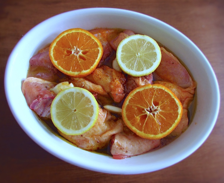 Chicken on a baking dish seasoned with salt, saffron, nutmeg, peeled crushed garlic, brown sugar, half lemon juice, half orange juice and olive oil, garnished with orange and lemon slices