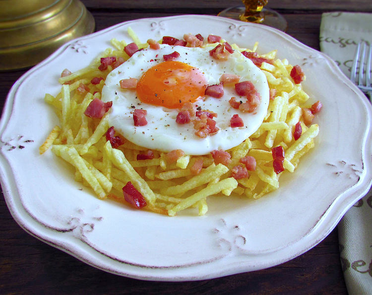 Fried egg with fries and small pieces of bacon on a plate