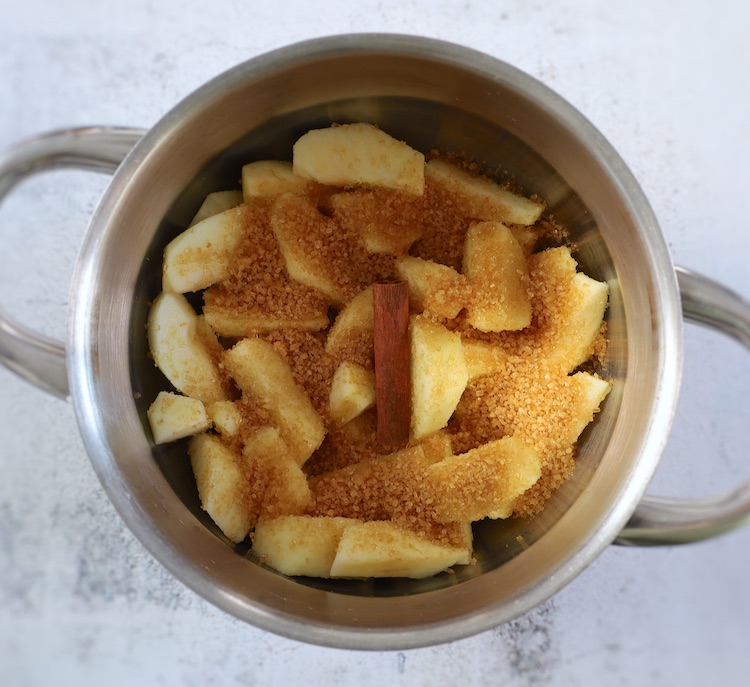 Apple slices, water, cinnamon stick and light brown sugar on a saucepan