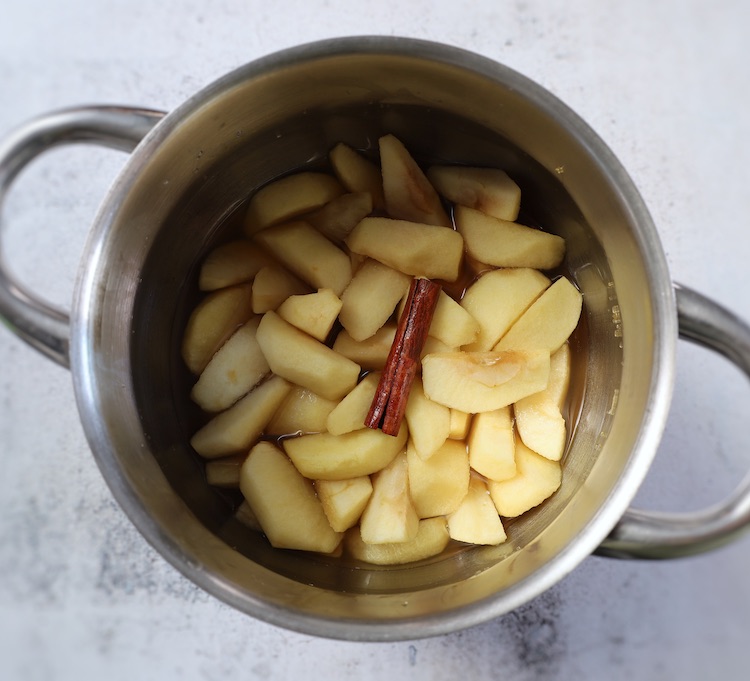 Apple slices, water, cinnamon stick and light brown sugar on a saucepan