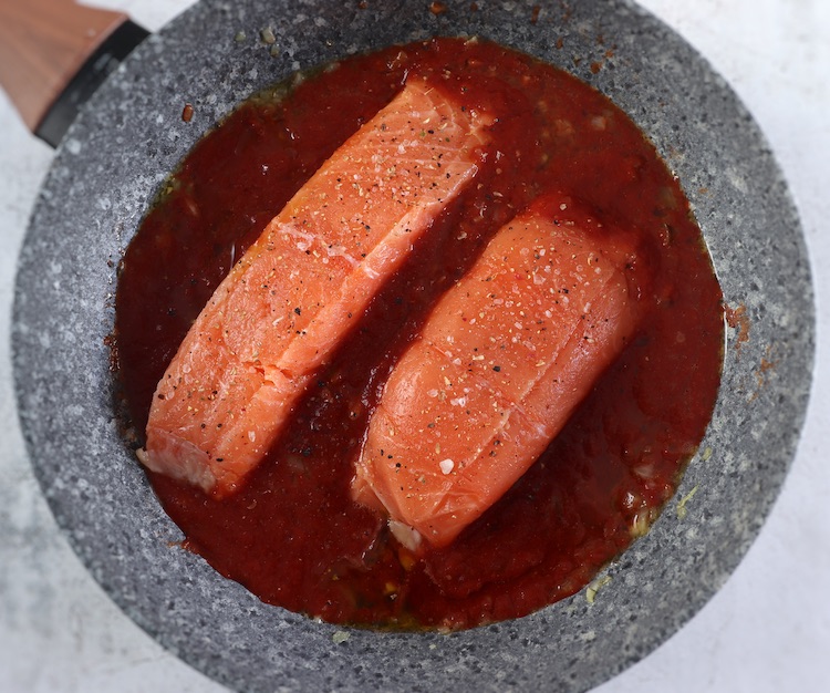 Salmon loins and tomato sauce on a frying pan