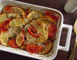 Baked hake with tomato and lemon on a baking dish