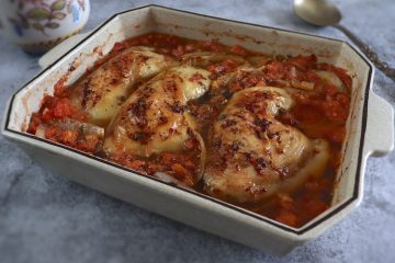 Baked chicken legs with tomato and oregano on a baking dish