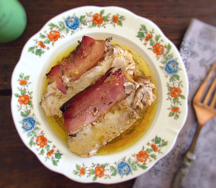 Slices of pork tenderloin in the oven with bacon on a plate