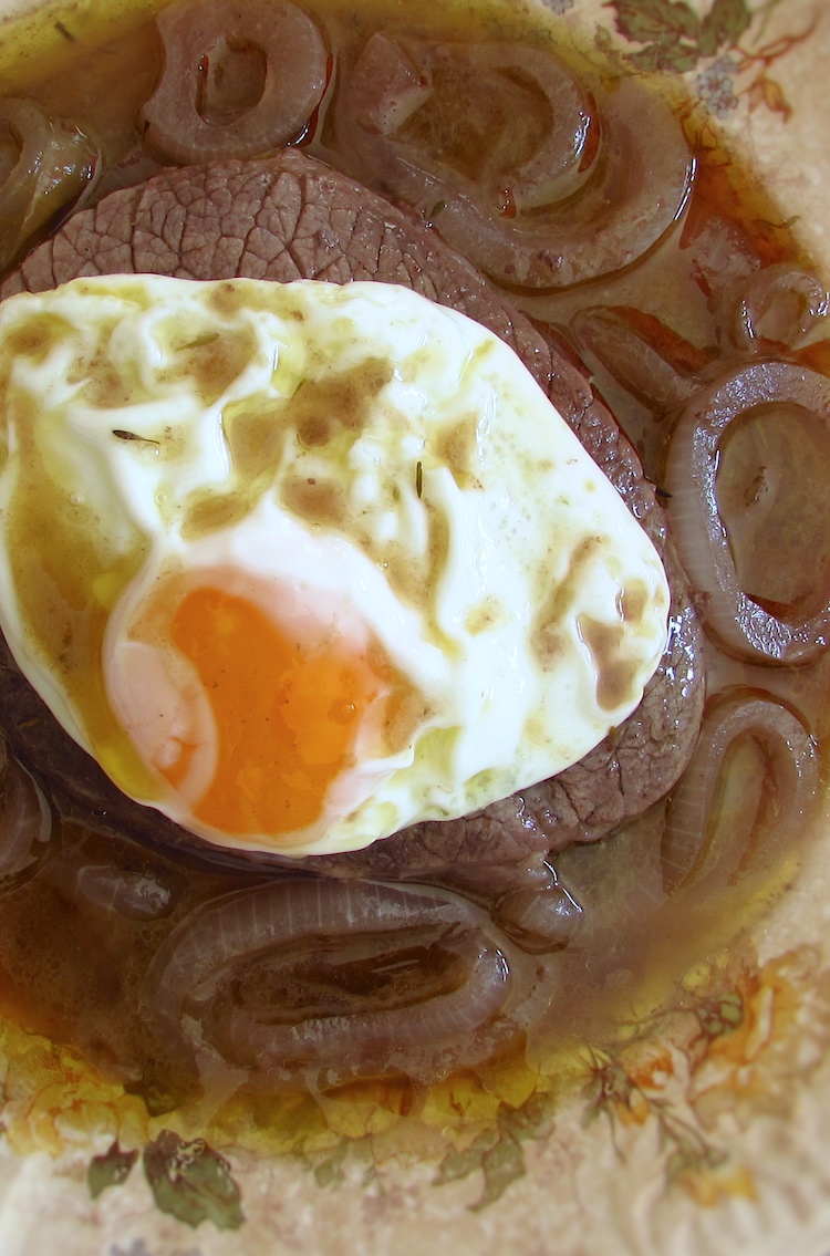 Stewed beef medallions with fried egg on a plate