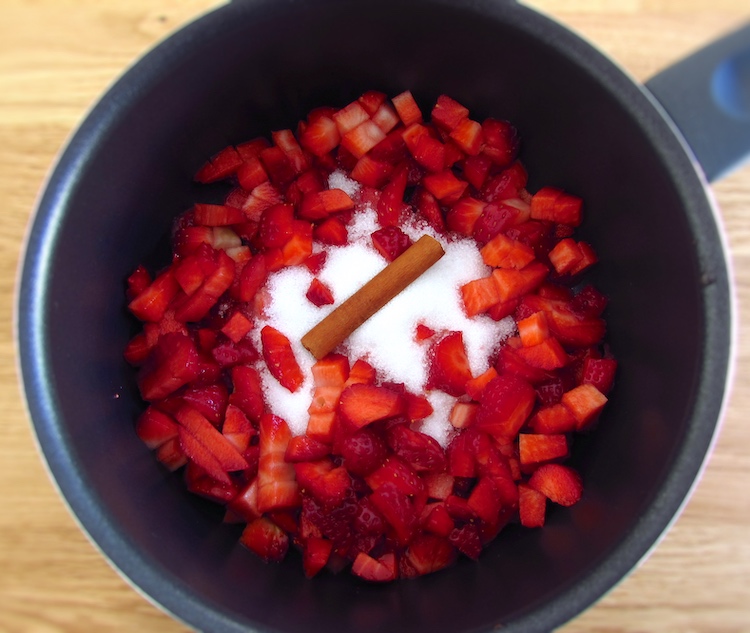 Strawberries cut into small pieces in a a saucepan together with sugar and a cinnamon stick