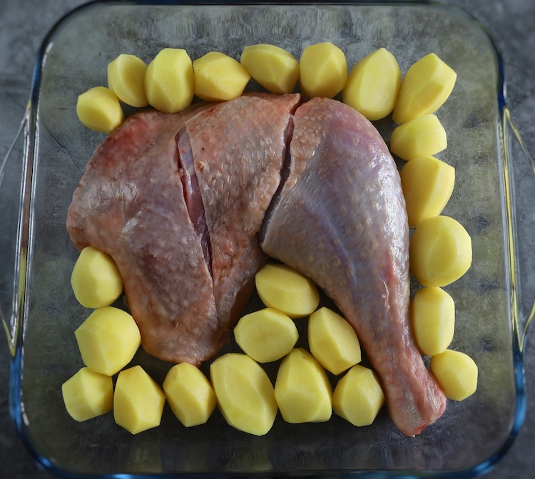 Turkey leg and peeled small potatoes on a glass baking dish