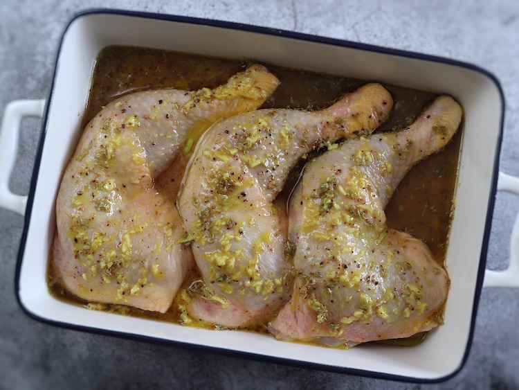 Chicken legs drizzled with sauce of mustard, olive oil, salt, lemon juice, oregano, grated garlic and nutmeg on a baking dish