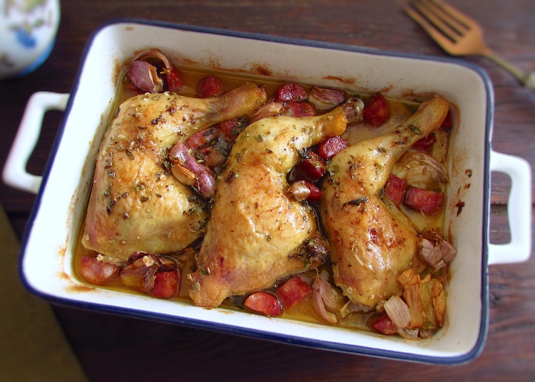 Roasted chicken legs with chouriço and garlic on a baking dish