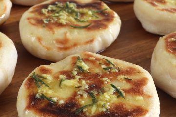 Pão pita caseiro com molho de azeite numa tábua de madeira redonda