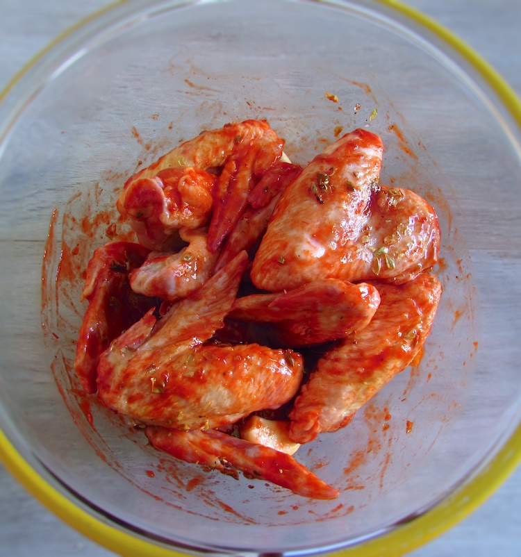 Chicken wings in a large dish bowl seasoned with a little salt, pepper, honey, oregano, saffron, nutmeg and peeled garlic