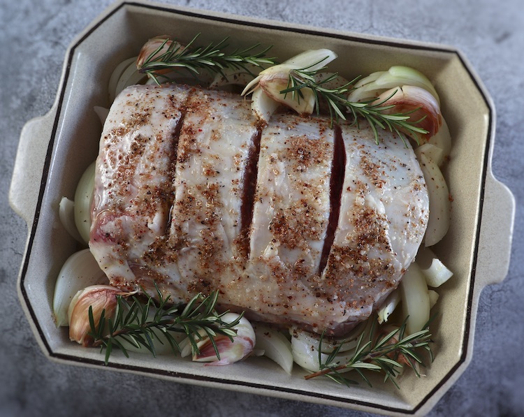Pork loin with onion seasoned with salt, pepper, nutmeg, rosemary, unpeeled crushed garlic and olive oil on a baking dish