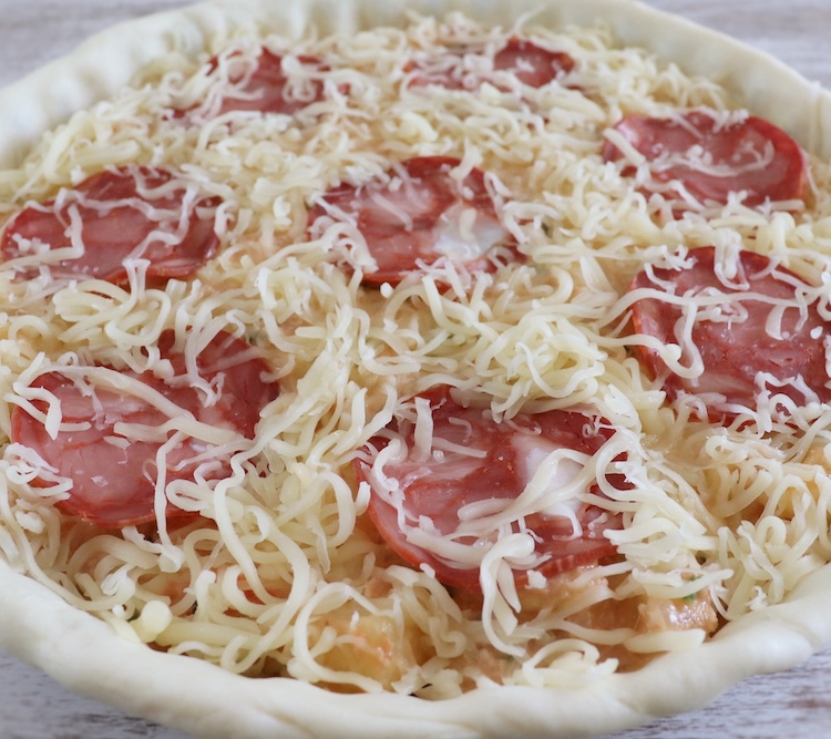 Pie filled with tuna, potato, slices of Portuguese sausage and grated cheese in a pie pan