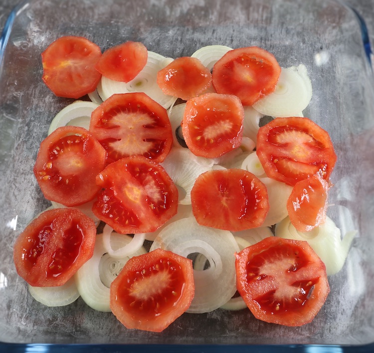 Sliced onion and tomato in a glass baking dish