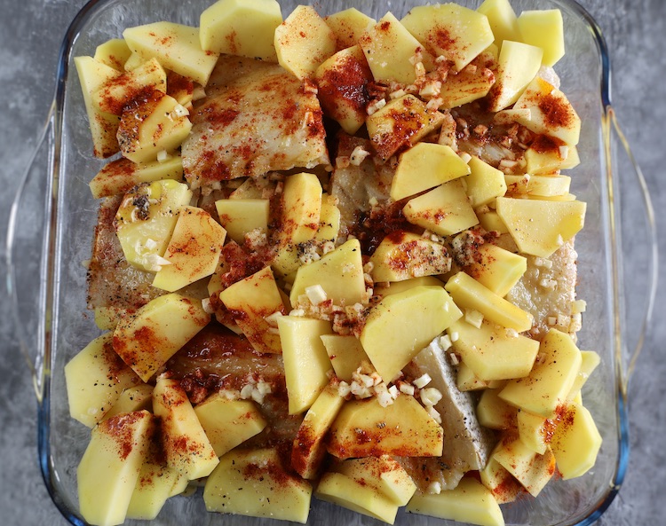 Cod with potatoes seasoned with tomato, onion, spices, olive oil and white wine in a glass baking dish